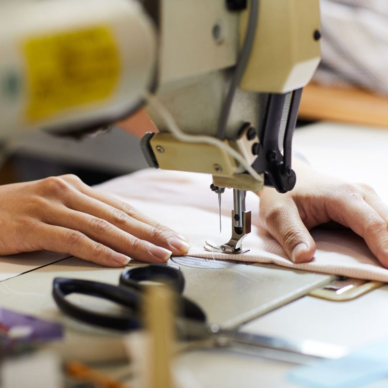 Close-up of woman working with fabric and she sewing with the help of sewing machine at her workplace